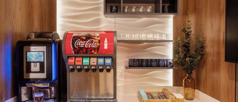 A coffee machine, a Coca-Cola dispenser, and a glass display with various items on a counter.