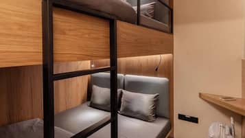 Habitación con literas de madera, ropa de cama gris y una mesita de noche pequeña con una lámpara.