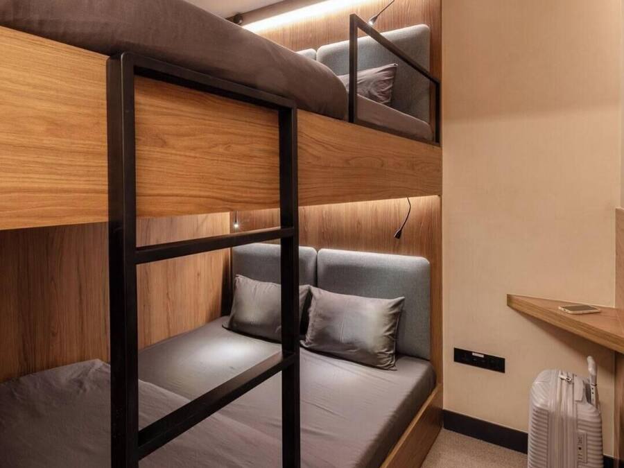 Une chambre avec un lit superposé doté d’une structure en bois, d’une literie grise et d’une petite table de chevet avec une lampe.