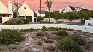Un quartier résidentiel avec des maisons blanches, un chemin pavé et un ciel au coucher du soleil.