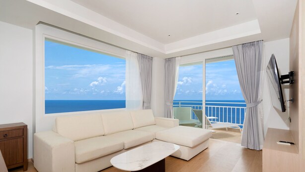 Un soggiorno moderno con una grande finestra, un divano bianco, un tavolino da caffè e un balcone con vista sul mare.