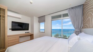 Una camera d'albergo moderna con un letto grande, una televisione a schermo piatto, un balcone vista mare e un armadio in legno.