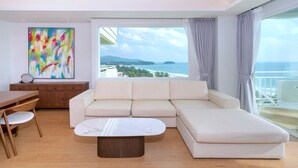 Un soggiorno moderno con una grande finestra, un divano beige, un tavolo da pranzo in legno e un quadro astratto colorato.