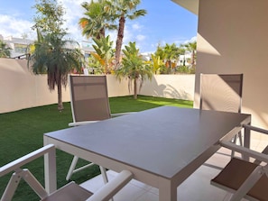 Un patio con una mesa, sillas, un pequeño césped y palmeras.
