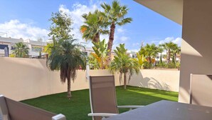 Une terrasse avec une table et des chaises, entourée d’une pelouse bien entretenue et de palmiers.