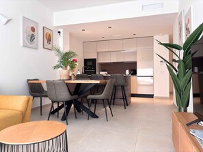 A modern kitchen with a dining area, featuring a central island, chairs, and a potted plant.