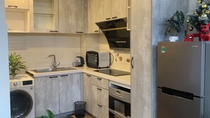 A modern kitchen with a stainless steel refrigerator, a microwave, and a built-in oven. There is a sink with a faucet, a countertop with a toaster, and a potted plant. - Holly Apartment - Truc Bach Lake (Hanoi)