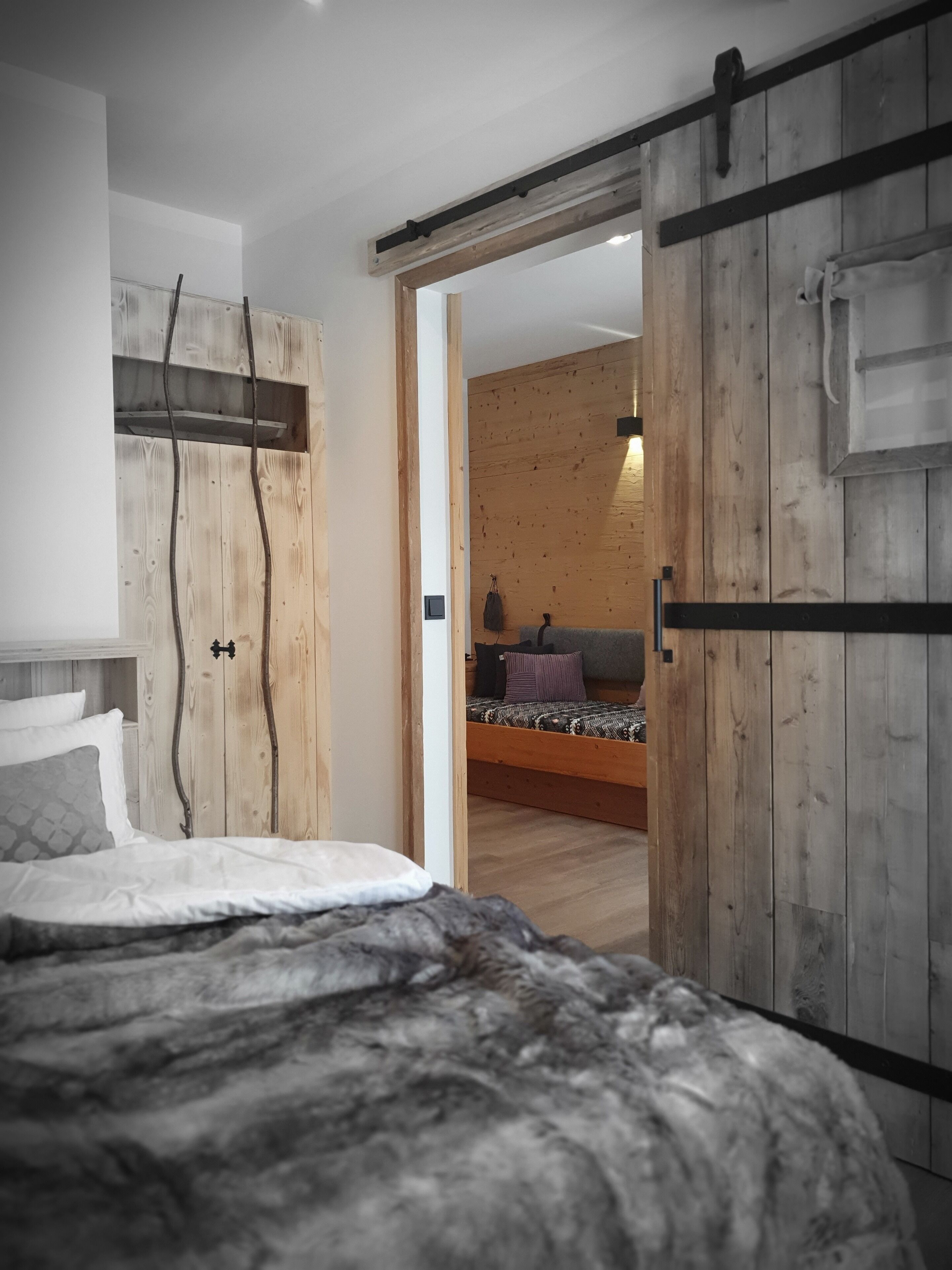 A bedroom with a bed, wooden wardrobe, and a view into another room.