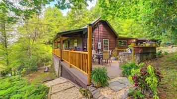 Une cabane en bois dotée d’une terrasse, entourée d’une végétation luxuriante et bordée d’un sentier en pierre.
