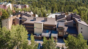 A residential complex with multiple buildings, including a prominent building labeled "VAIL INTERNATIONAL CONDOMINIUMS." The complex is surrounded by dense forest and hills in the background.