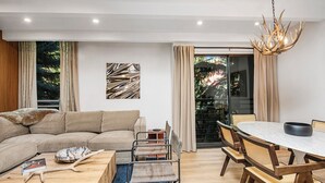 A modern living room with a sectional sofa, a dining table with chairs, a coffee table, and a chandelier.