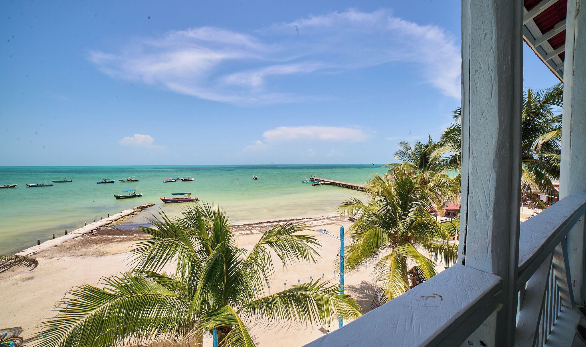 A beach view with boats, palm trees, and a pier.