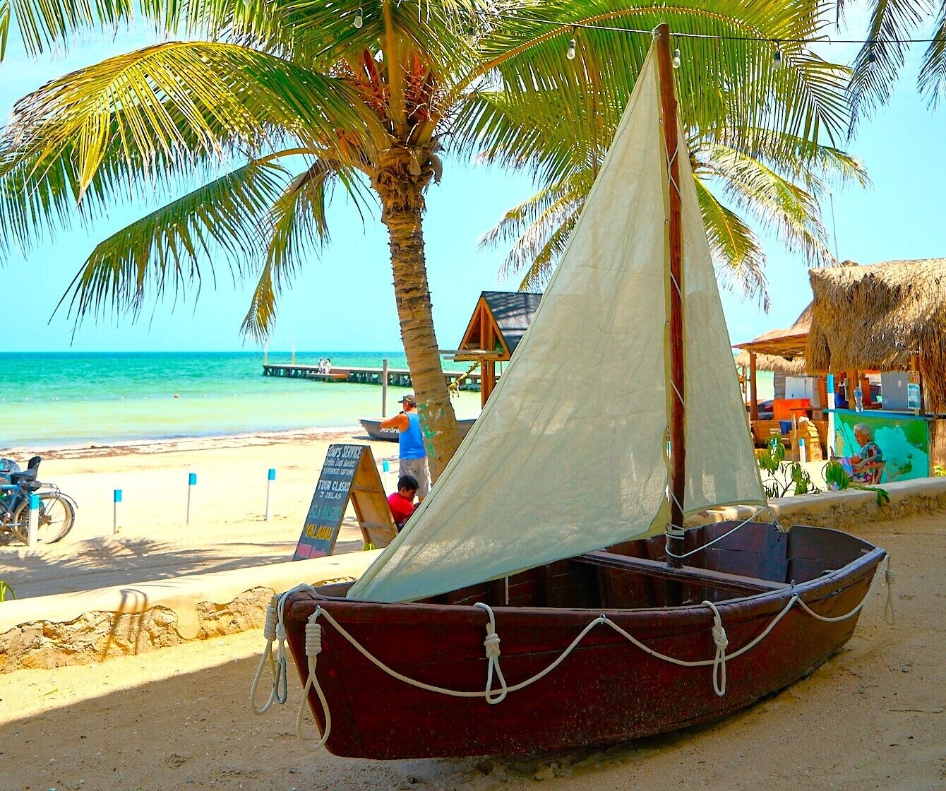 Una pequeña embarcación en una playa arenosa con palmeras y un cielo azul despejado al fondo.