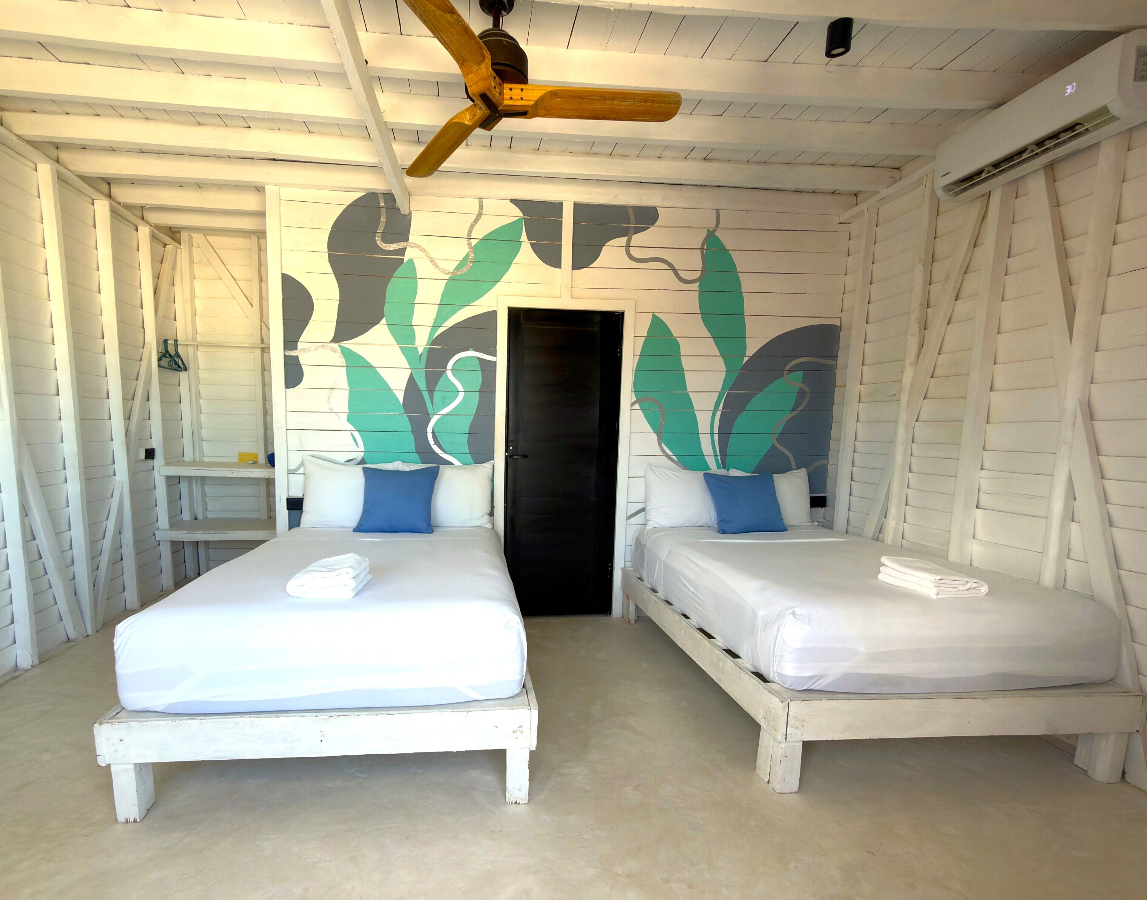 Una habitación con dos camas, un ventilador de techo y un mural en la pared.