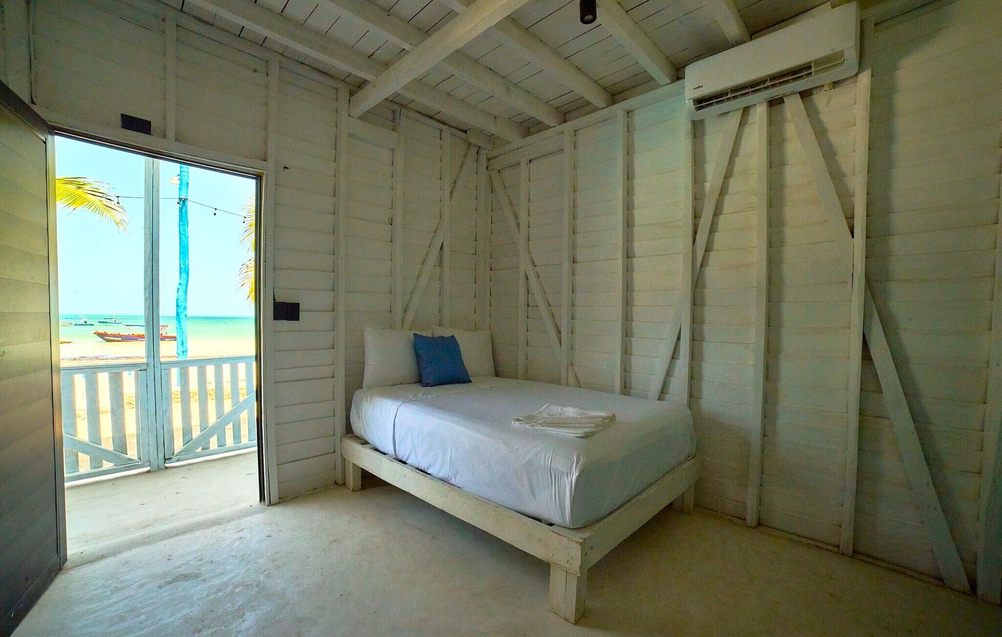 A single bed in a room with a view of the beach through a door.