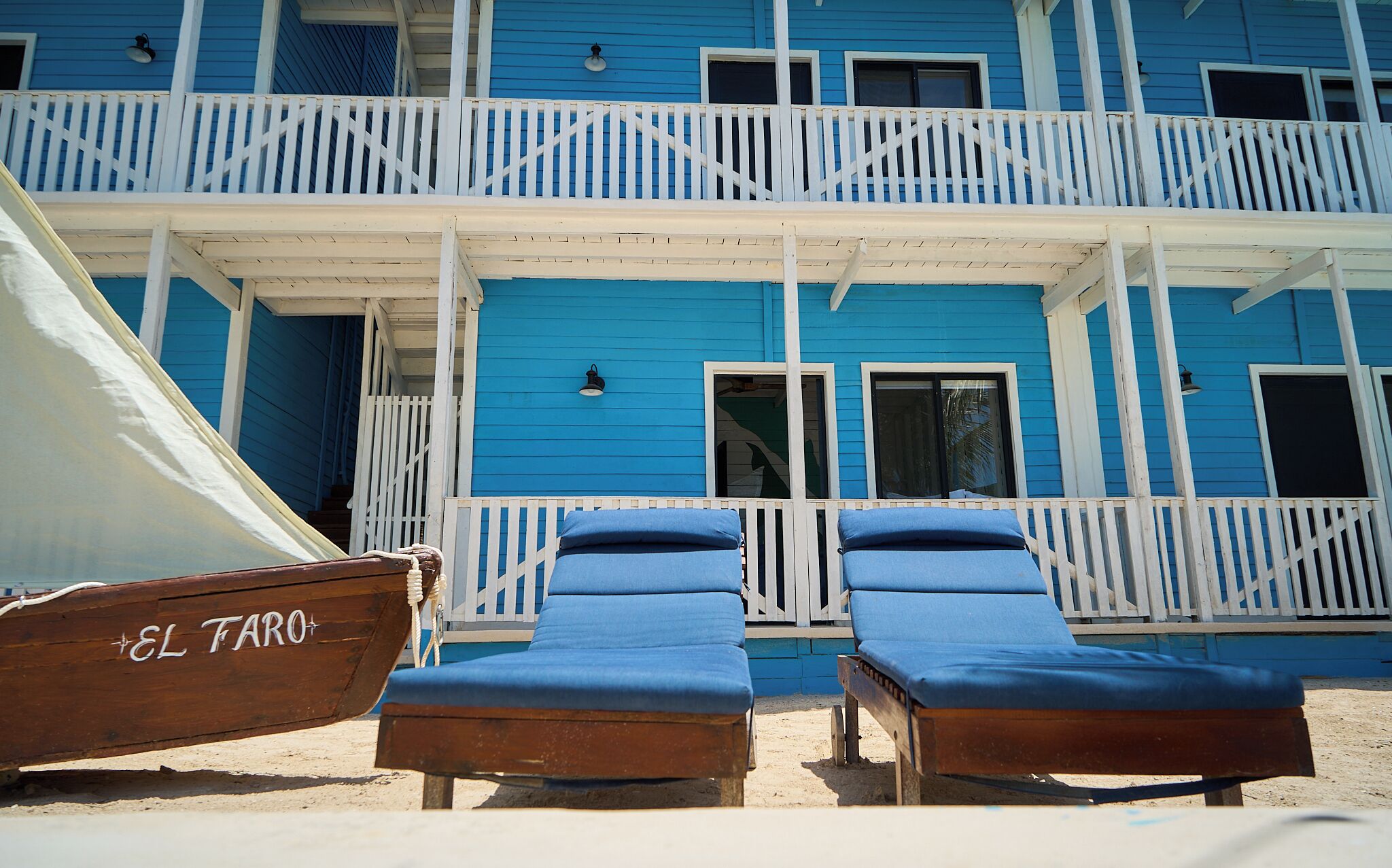 A beachfront building with a balcony, two lounge chairs, and a boat named "EL TARO" in the foreground.