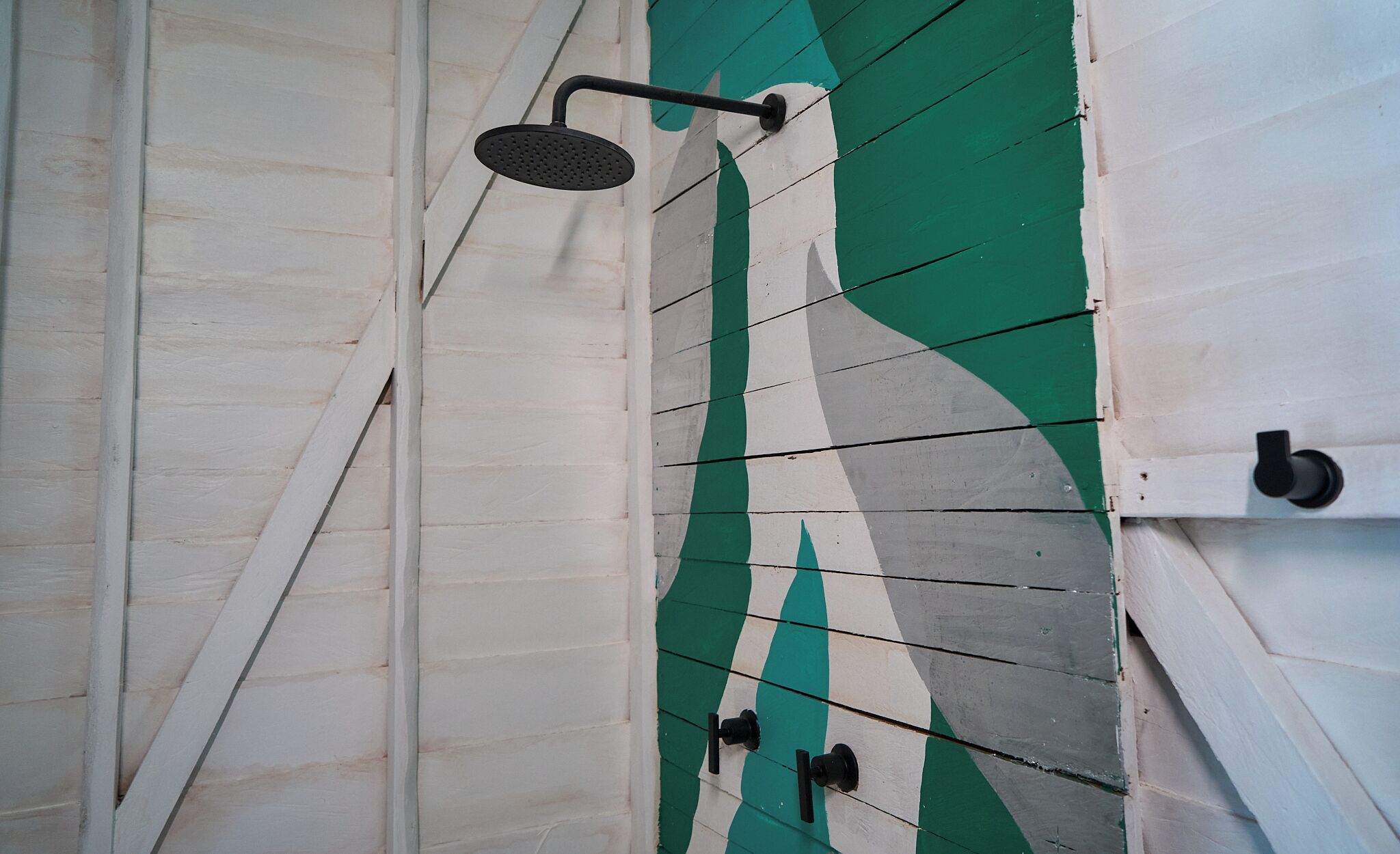 A shower with a handheld showerhead and a wall with a green and white pattern.