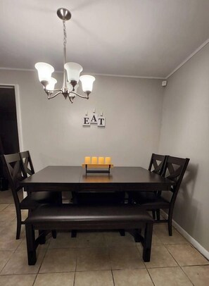 Un coin repas avec une table en bois foncé, quatre chaises, un banc et un lustre.