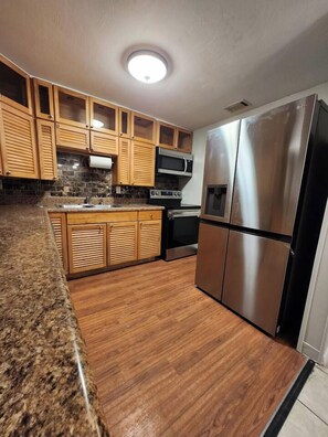 Una cocina con armarios de madera, un refrigerador de acero inoxidable y una encimera de granito.