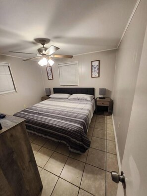 Une chambre à coucher avec un lit, des tables de chevet, un ventilateur de plafond et une petite table de nuit.