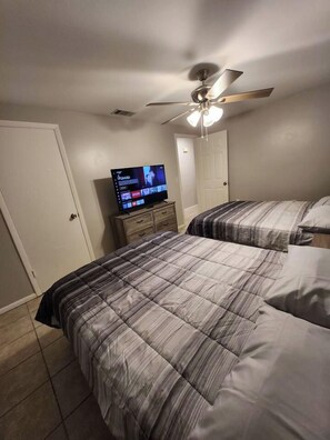 A bedroom with two beds, a ceiling fan, a television on a dresser, and a door. - Central 3 Bedroom AC Home with Gameroom

 (Lakeland)