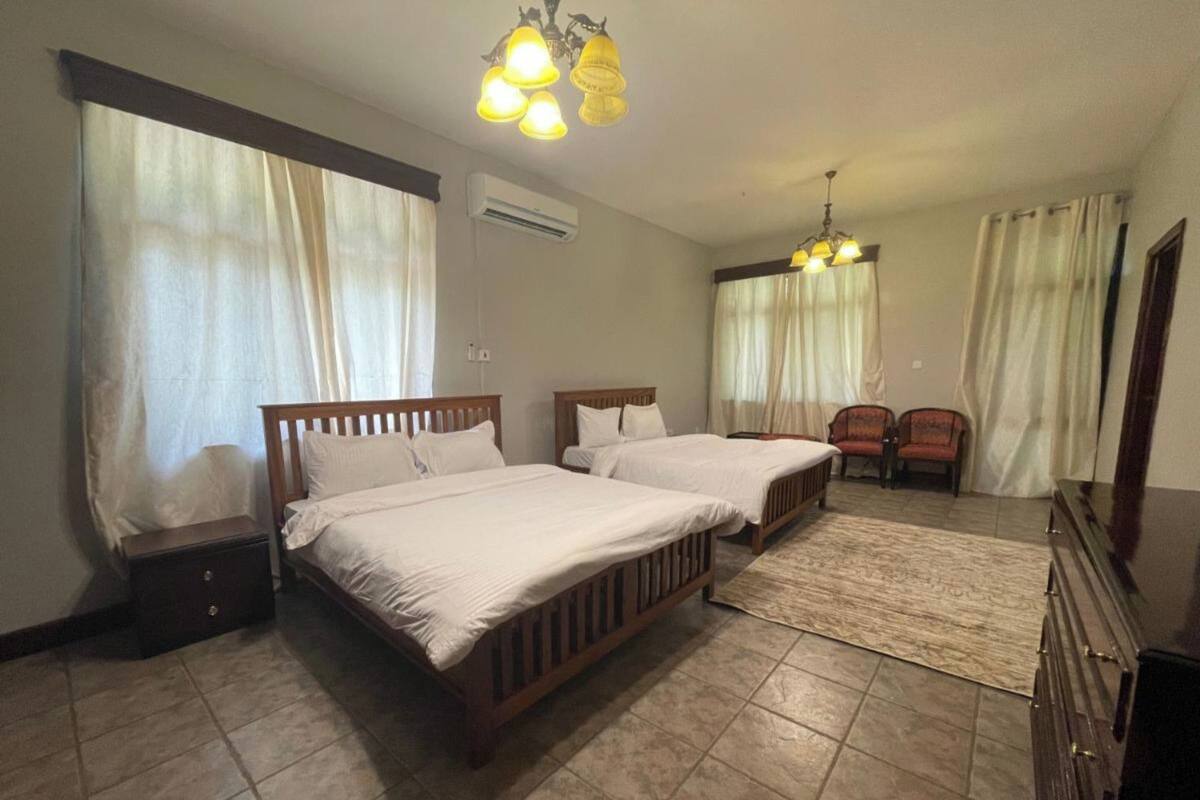 Quarto de hotel com duas camas, uma escrivaninha, uma cadeira e um armário.