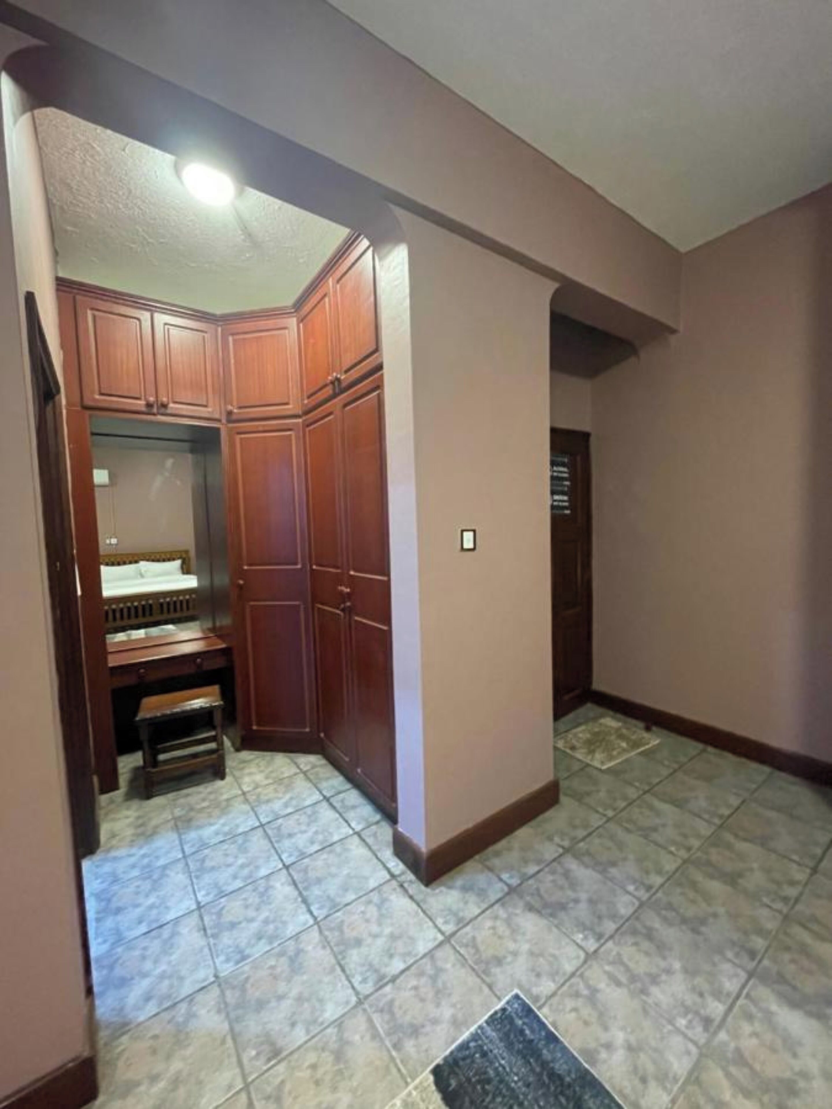 Quarto com um armário de madeira, um banco e um chão ladrilhado.