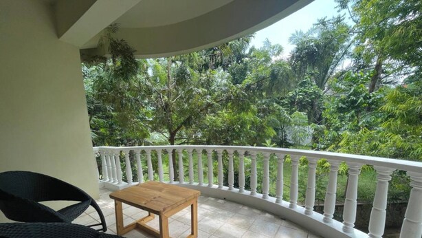 Een balkon met een witte balustrade, een houten tafel en twee rieten stoelen.