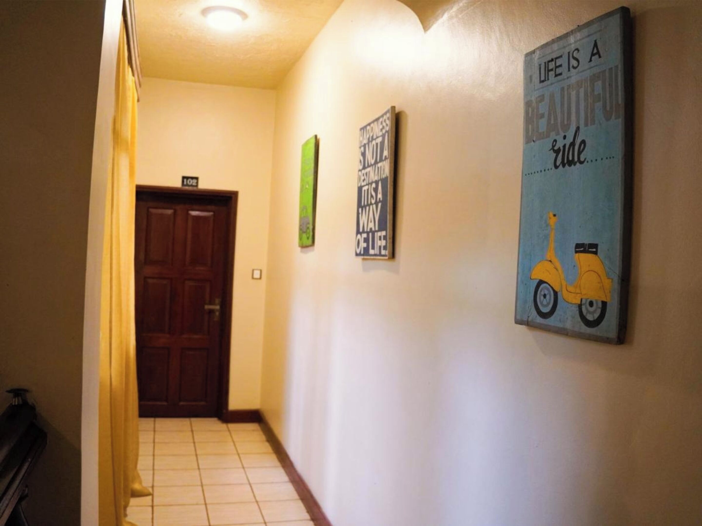 Un pasillo con una puerta de madera, un cartel que indica la habitación 102 y tres carteles de motivación en la pared.