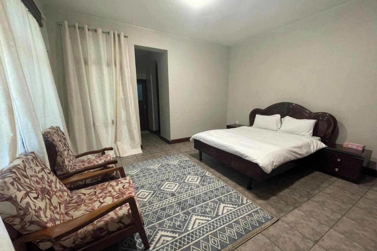 Quarto com cama, uma cadeira, mesa de cabeceira e tapete estampado.