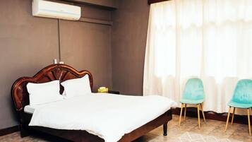 A bedroom with a wooden bed, a nightstand, two chairs, and a window with curtains.