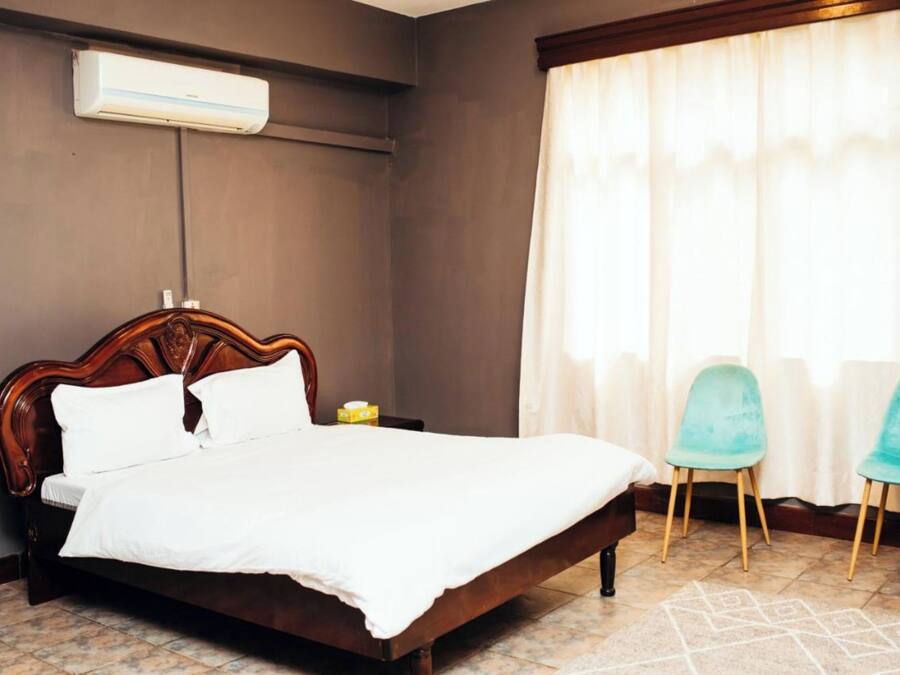 A bedroom with a wooden bed, a nightstand, two chairs, and a window with curtains.
