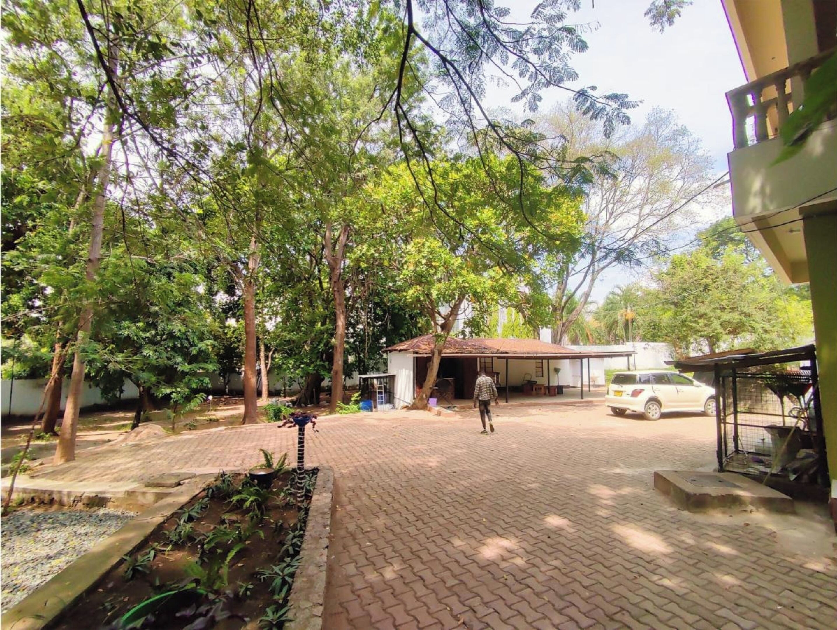 Un patio empedrado con árboles, un edificio pequeño y un coche estacionado.