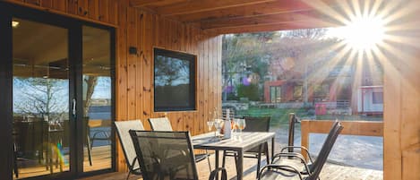 En træterrasse med et bord og stole, et fjernsyn monteret på væggen og udsigt til det fri.