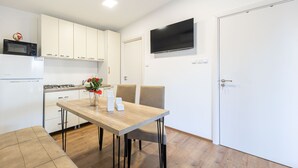 Eine moderne Küche mit weißen Schränken, einem Holztisch und einem an der Wand befestigten Flachbildfernseher.