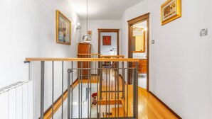 A staircase with a wooden handrail and metal balusters, leading to an upper floor. There are framed artworks on the walls and a wooden cabinet in the hallway. - Villa Karla in Poljane (Opatija)
