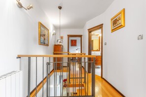 A staircase with a wooden handrail and metal balusters, leading to an upper floor. There are framed artworks on the walls and a wooden cabinet in the hallway. - Villa Karla in Poljane (Opatija)