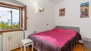A bedroom with a bed, a window, a radiator, a bench, and two paintings on the wall. - Villa Karla in Poljane (Opatija)