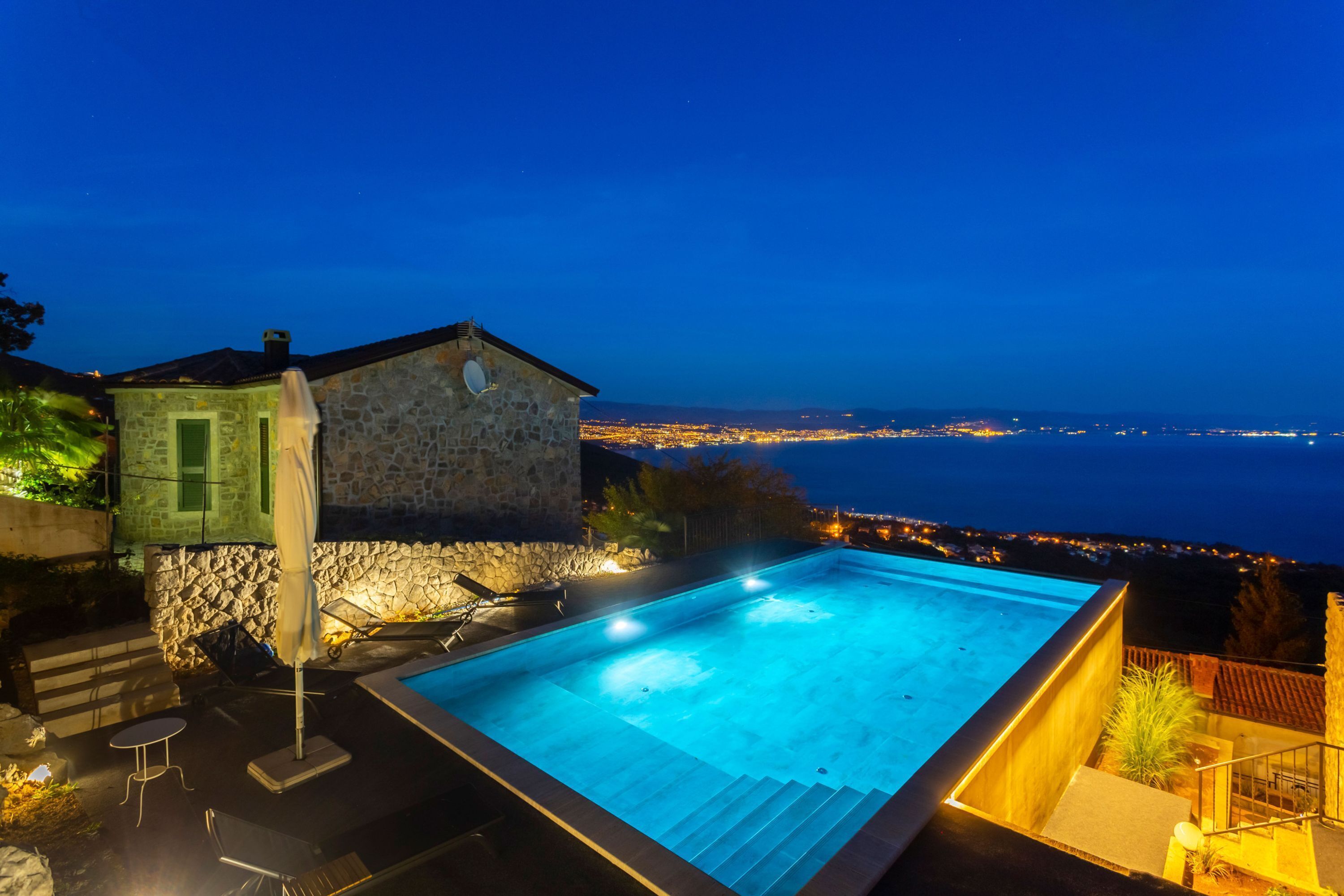 A stone building with a swimming pool, outdoor seating, and a view of the city at night.