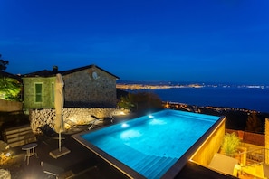 Un edificio in pietra con piscina, posti a sedere all'aperto e vista sulla città di notte.