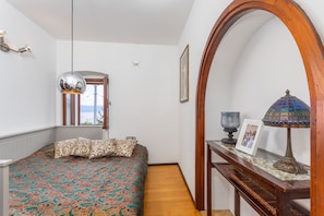 A bedroom with a patterned bedspread, a wooden arched doorway, a bedside table with a lamp, and a framed picture. - Villa Karla in Poljane (Opatija)