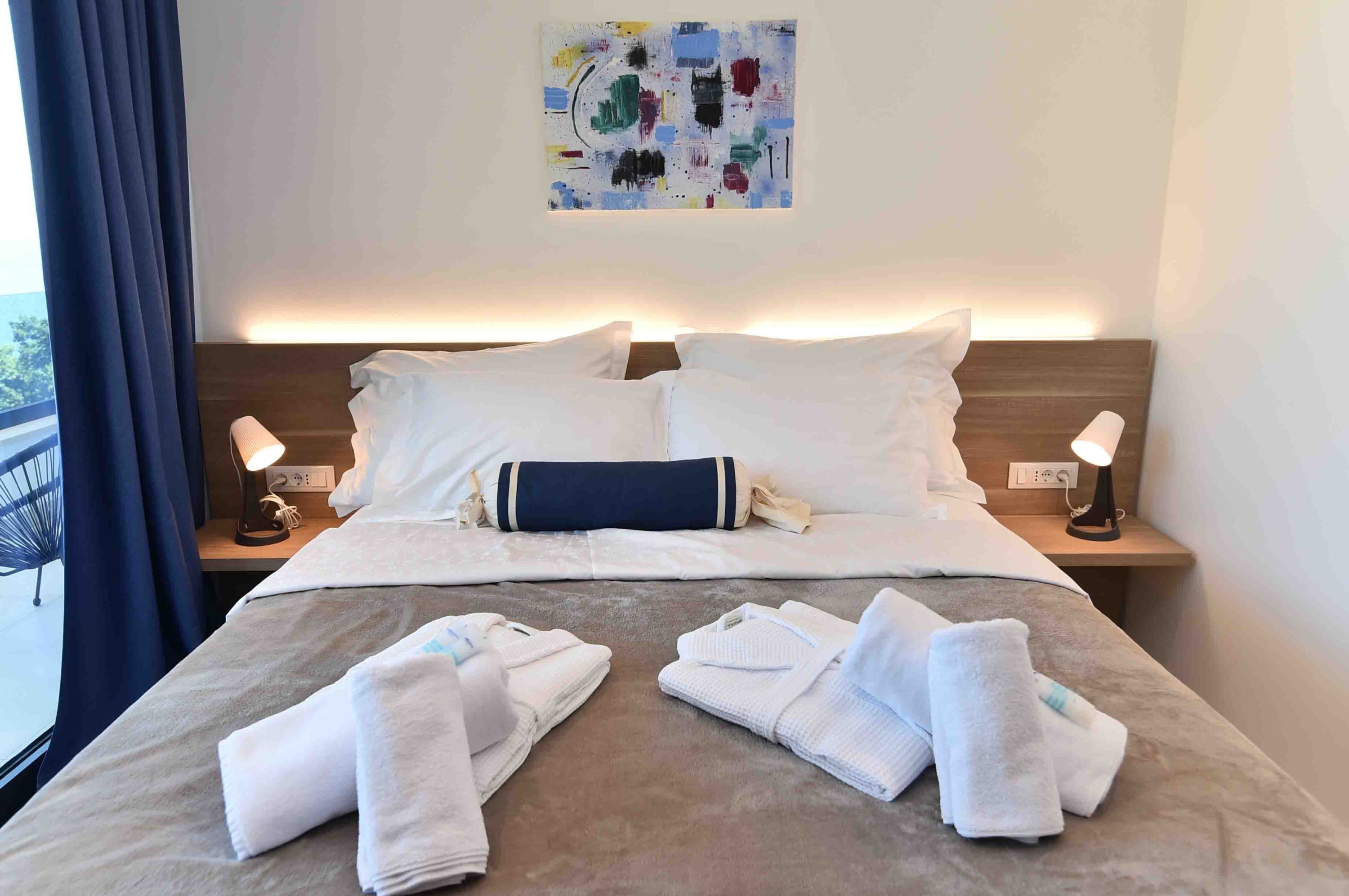 Ein Hotelzimmer mit einem Bett, zwei Nachttischlampen, einem Bild an der Wand und Handtüchern auf dem Bett.