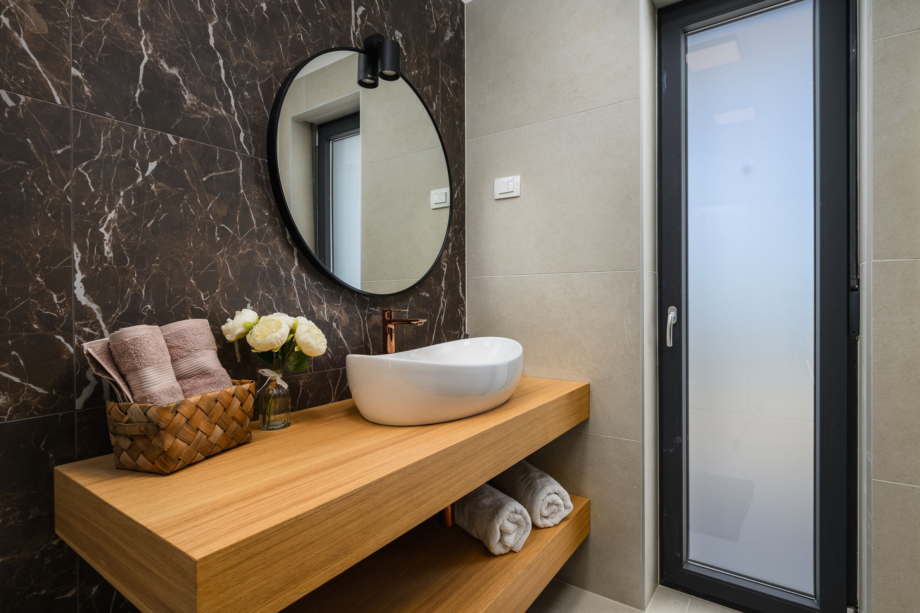 Un baño moderno con salpicadero de mármol, tocador de madera, lavabo blanco y un espejo grande.