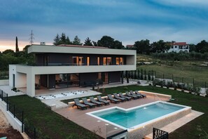 Uma casa moderna de dois andares com piscina, área de estar externa e um jardim bem cuidado.