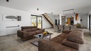 Een moderne woonkamer met een bruine bank, een salontafel en een trap naar een eetgedeelte.
