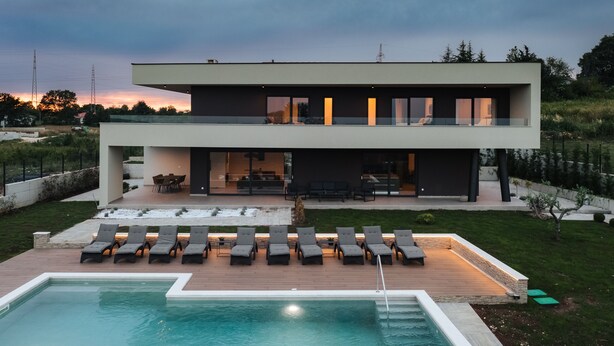 Een modern huis met twee verdiepingen, een zwembad, buitenzitplaatsen en een verzorgde tuin.