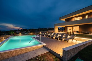Uma área moderna de piscina ao ar livre com espreguiçadeiras e piscina, rodeada por um deck de madeira e paredes de pedra.