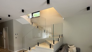 Ein modernes Wohnzimmer mit einem grauen Sofa, einem Boden mit geometrischem Muster und einer Treppe mit Glasgeländern.