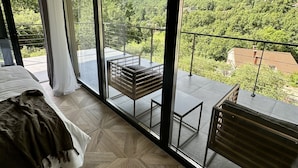 Ein modernes Schlafzimmer mit einer großen Schiebeglastür, die auf einen Balkon mit Blick auf eine malerische Berglandschaft führt.