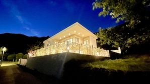 Ein modernes Haus mit Balkon, umgeben von Bäumen und einem Berg im Hintergrund.